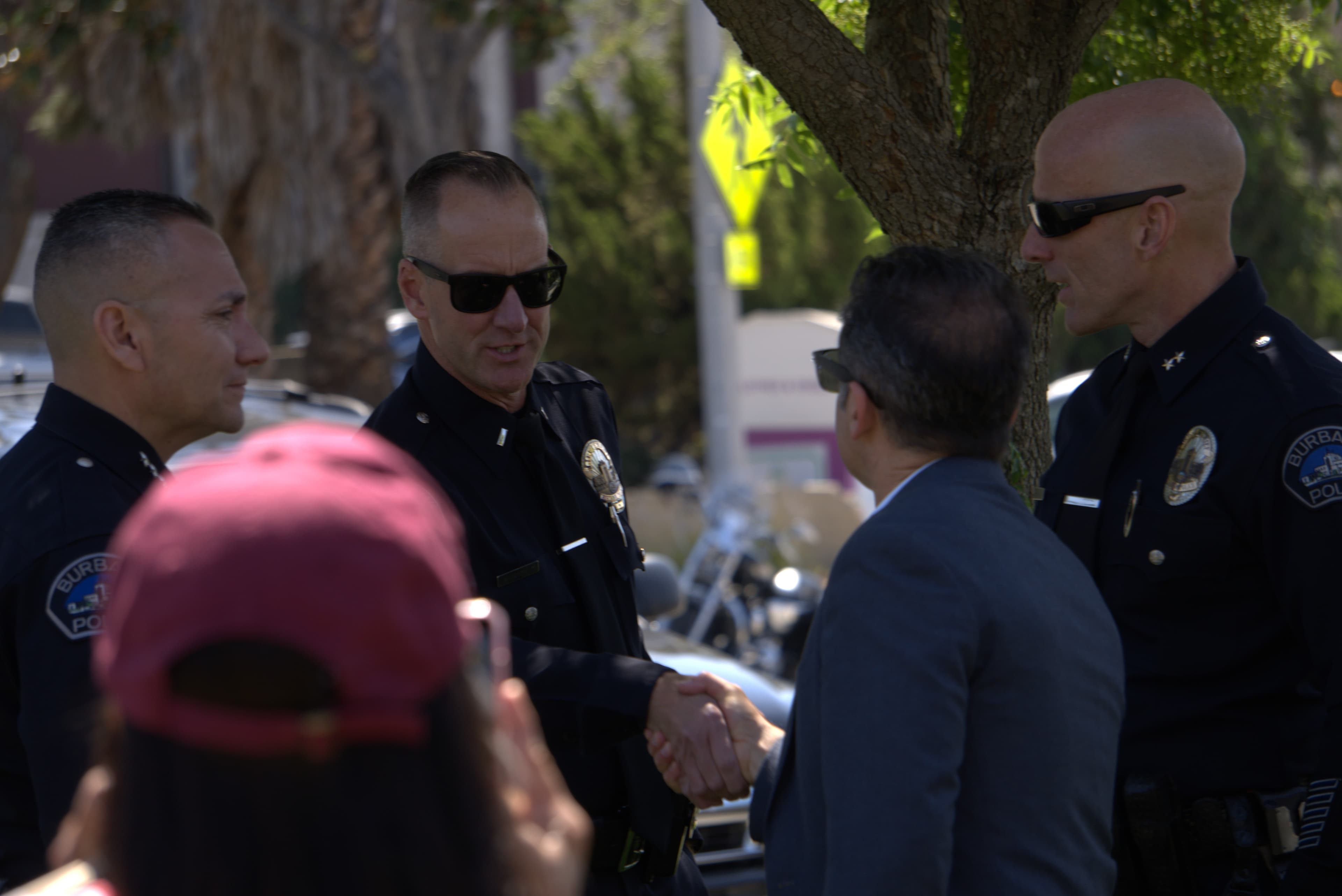 Burbank police officer in sunglasses shakes hands with a man in a suit outdoors.