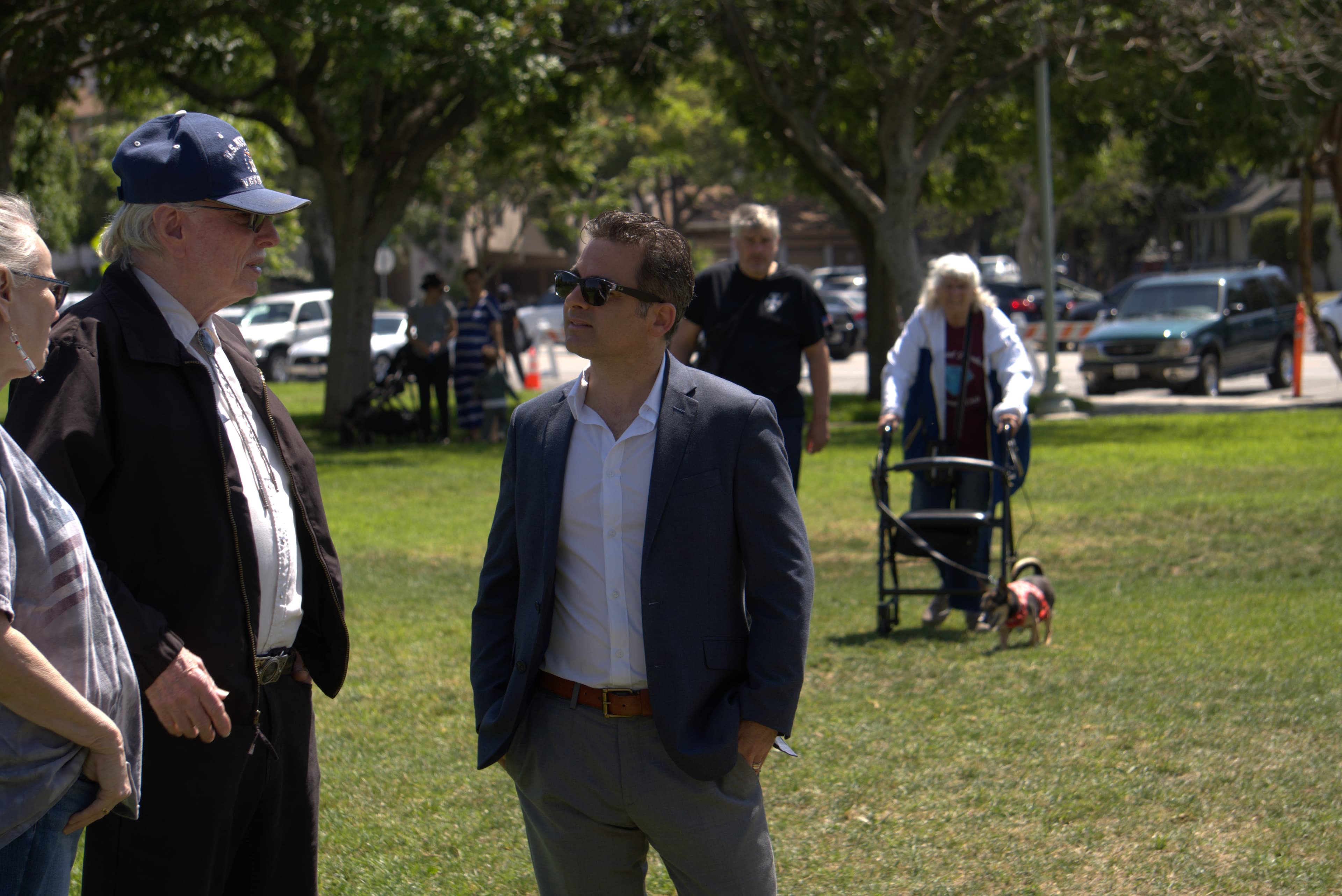 Man in a blue blazer and sunglasses talks to an older veteran in a park.