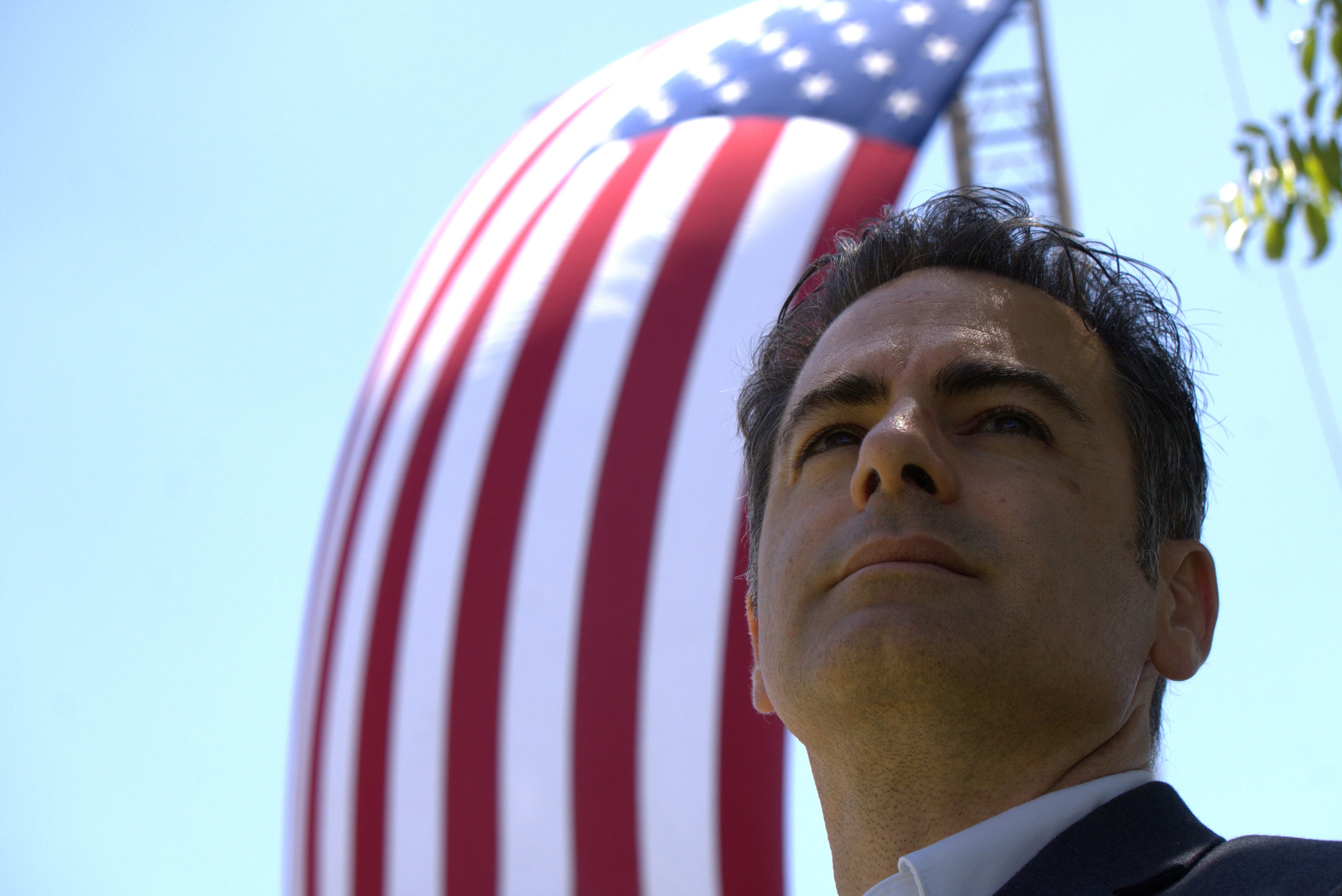 Man in a suit gazes upward with a large, billowing American flag in the background.