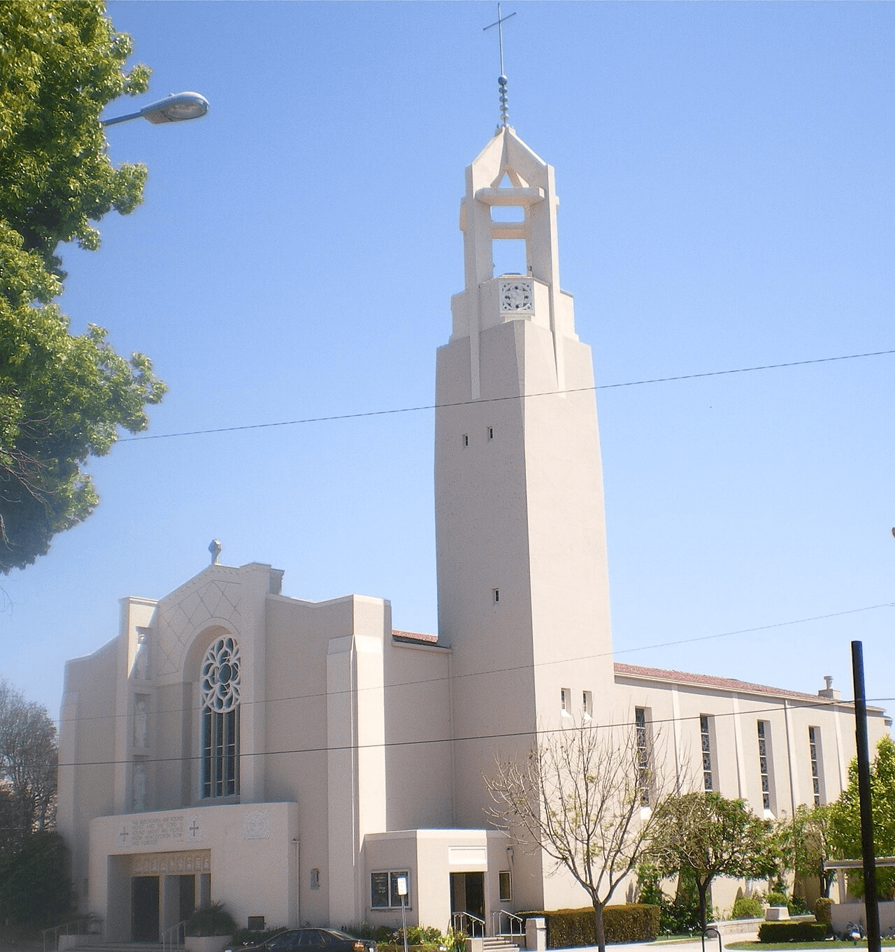 Modern beige church with a tall, slender bell tower and cross against a clear sky.